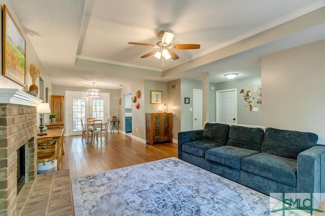 living area featuring a ceiling fan, crown molding, light wood-type flooring, a fireplace, and baseboards