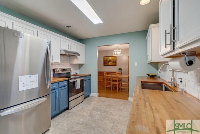 kitchen featuring under cabinet range hood, blue cabinets, a sink, butcher block countertops, and appliances with stainless steel finishes