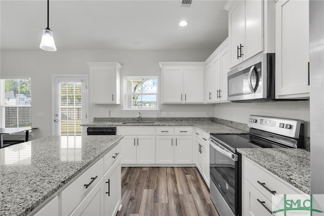 kitchen featuring wood finished floors, hanging light fixtures, a sink, stainless steel appliances, and white cabinetry