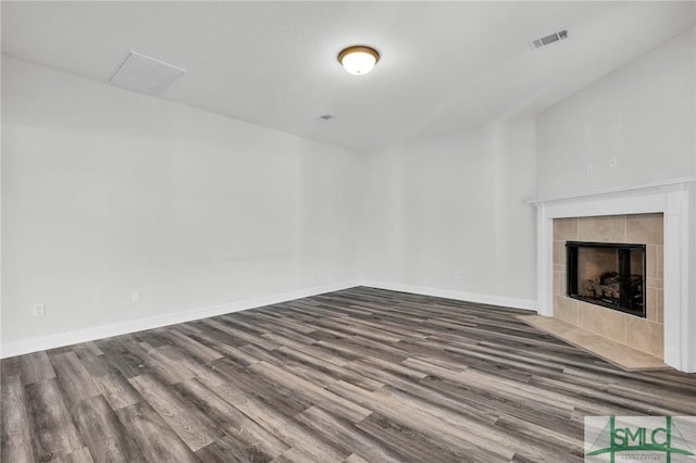 unfurnished living room featuring baseboards, wood finished floors, visible vents, and a tiled fireplace