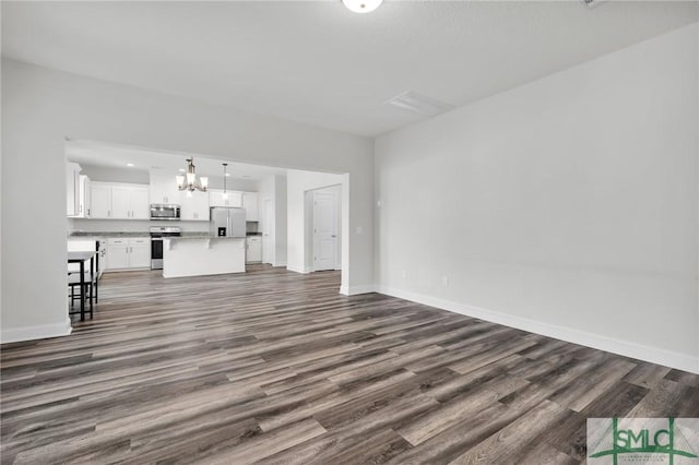 unfurnished living room featuring dark wood finished floors, baseboards, and a notable chandelier