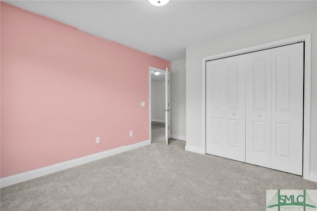 unfurnished bedroom with carpet floors, a closet, a textured ceiling, and baseboards