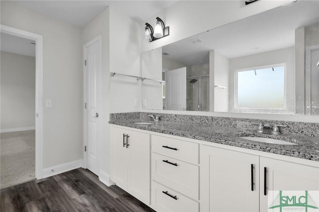 full bath with a sink, double vanity, a stall shower, baseboards, and wood finished floors