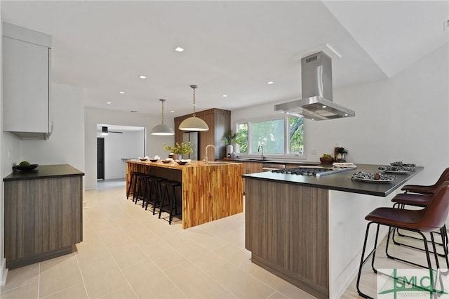 kitchen featuring a peninsula, stainless steel gas stovetop, a breakfast bar area, island range hood, and dark countertops