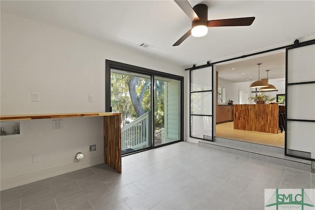spare room with a barn door, visible vents, ceiling fan, light tile patterned floors, and baseboards