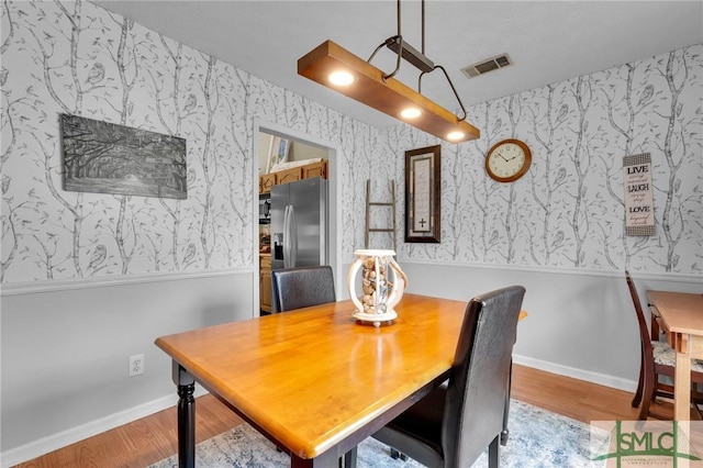 dining room with wallpapered walls, wood finished floors, visible vents, and baseboards