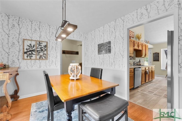 dining space featuring wallpapered walls, light wood-style flooring, and a wainscoted wall