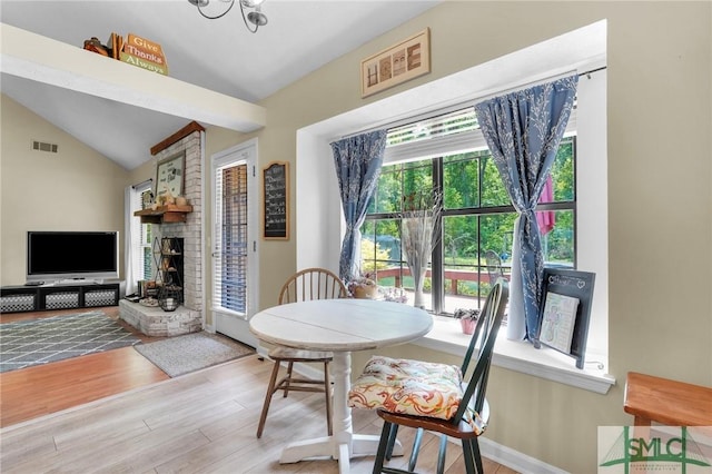 dining area with a fireplace, lofted ceiling, visible vents, and wood finished floors