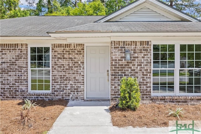 doorway to property with brick siding and a shingled roof