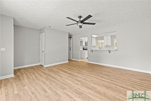 unfurnished living room featuring a textured ceiling, light wood finished floors, baseboards, and a ceiling fan