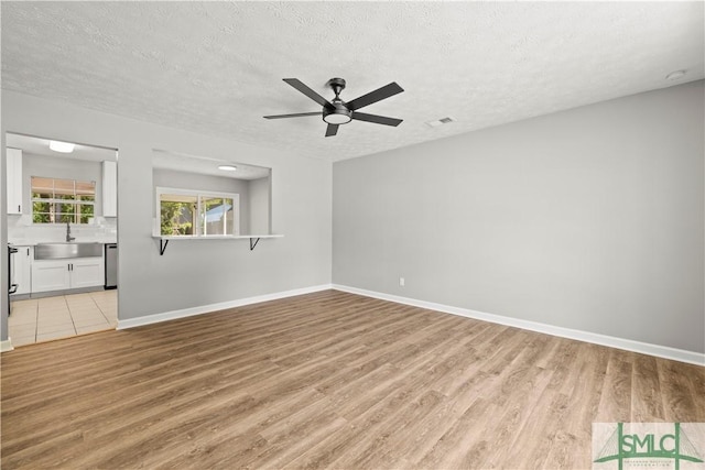 unfurnished living room featuring visible vents, a ceiling fan, a sink, light wood-type flooring, and a textured ceiling