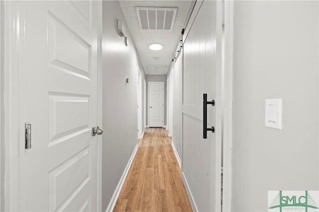 corridor featuring attic access, light wood-style floors, visible vents, and baseboards