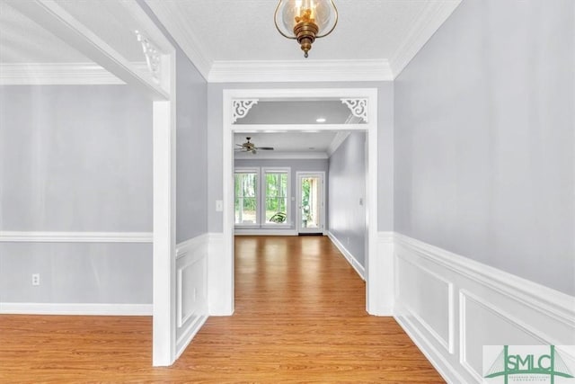 corridor featuring light wood finished floors, wainscoting, and crown molding