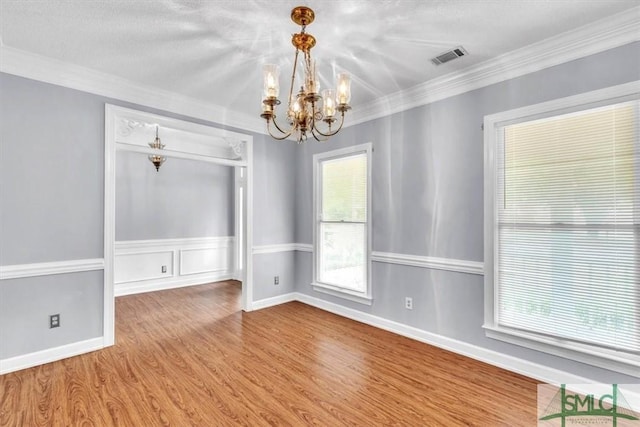 empty room featuring crown molding, wood finished floors, an inviting chandelier, baseboards, and visible vents