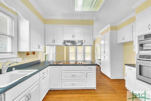 kitchen with under cabinet range hood, dark countertops, a sink, black electric stovetop, and a peninsula