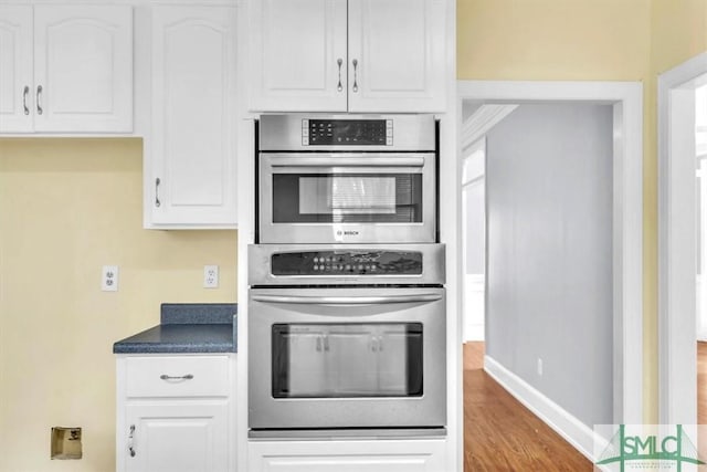kitchen featuring double oven, dark countertops, white cabinetry, and wood finished floors