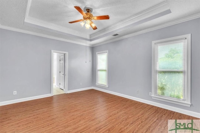 spare room featuring a tray ceiling, baseboards, light wood-style floors, a ceiling fan, and crown molding