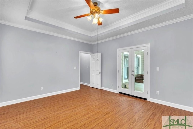 unfurnished room with a tray ceiling, wood finished floors, crown molding, and french doors