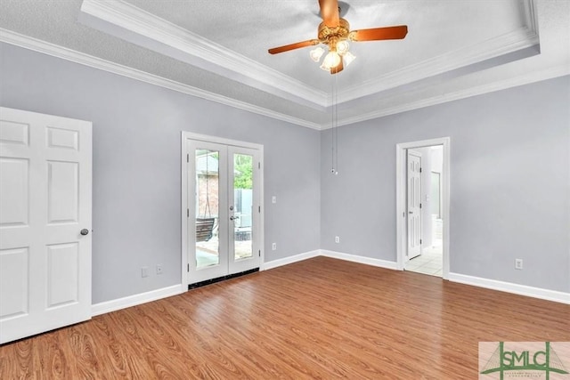 spare room with a tray ceiling, wood finished floors, crown molding, and french doors