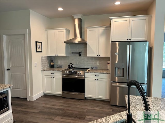 kitchen with wall chimney range hood, backsplash, appliances with stainless steel finishes, white cabinets, and dark wood-type flooring