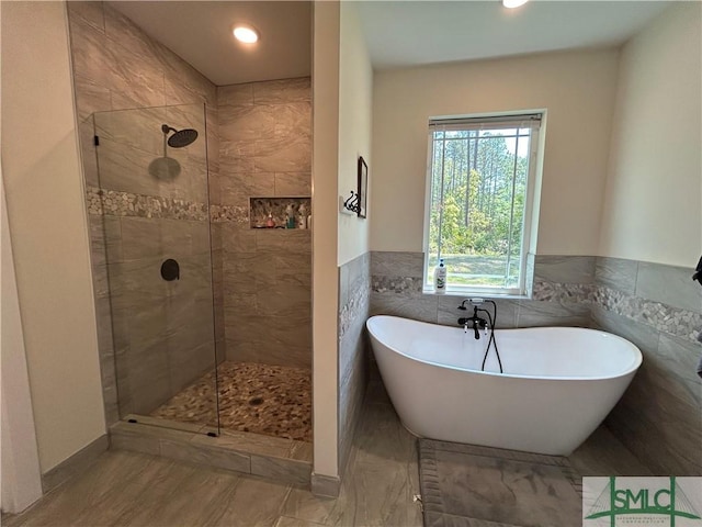 bathroom with a freestanding bath, a tile shower, a wainscoted wall, recessed lighting, and tile walls