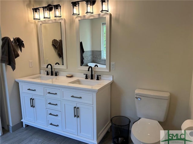 bathroom with a sink, baseboards, toilet, and double vanity