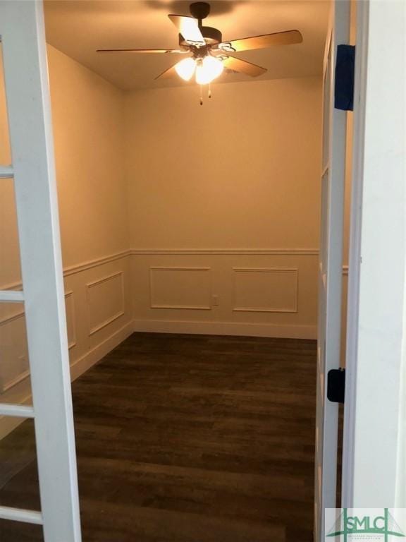 unfurnished room featuring a decorative wall, a ceiling fan, dark wood-style floors, and a wainscoted wall
