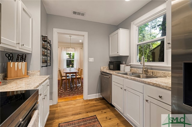 kitchen with stainless steel appliances, visible vents, a sink, light wood-style flooring, and white cabinetry