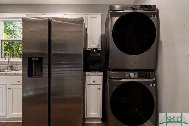 laundry room featuring wood finished floors, a sink, stacked washing maching and dryer, and laundry area
