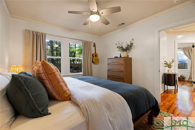 bedroom with ceiling fan, ornamental molding, wood finished floors, and visible vents
