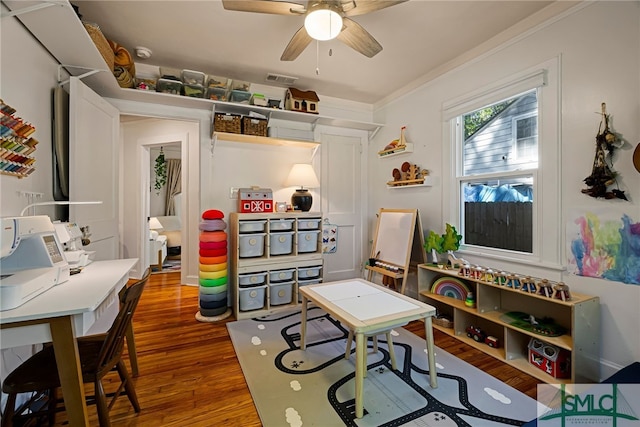 playroom with ceiling fan, ornamental molding, wood finished floors, and visible vents