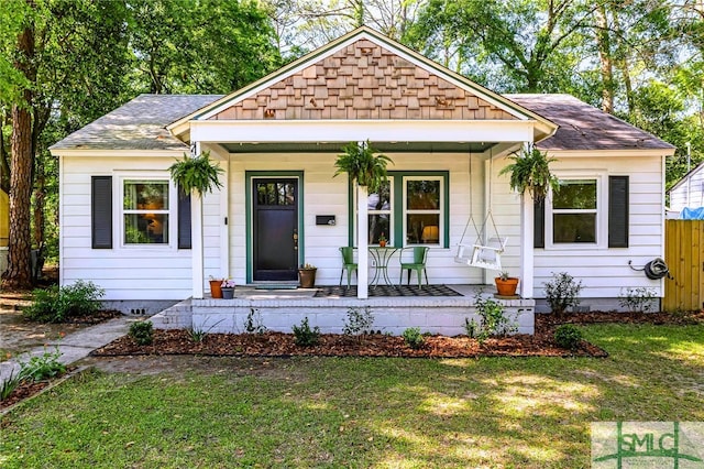view of front of home with a front lawn, a shingled roof, and covered porch