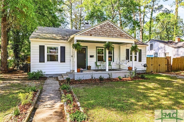 bungalow featuring a chimney, fence, a shingled roof, a front lawn, and covered porch
