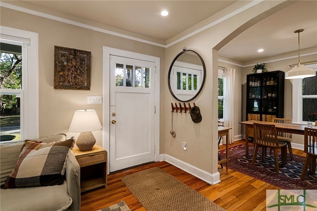 entrance foyer with arched walkways, crown molding, wood finished floors, and baseboards