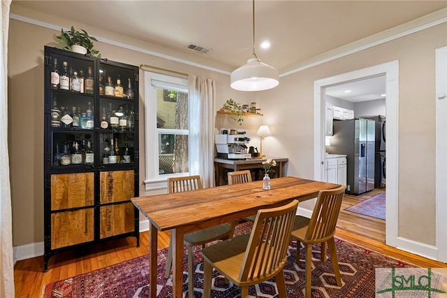 dining area featuring visible vents, light wood-style floors, and crown molding