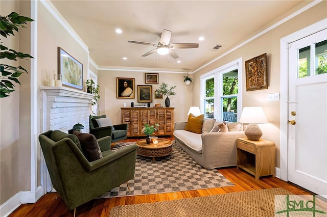 living room with visible vents, a ceiling fan, wood finished floors, a brick fireplace, and crown molding