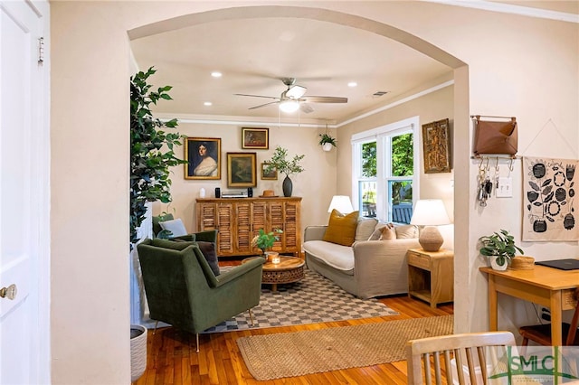 living area featuring hardwood / wood-style floors, visible vents, ornamental molding, arched walkways, and ceiling fan