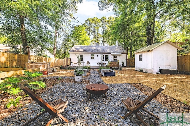 rear view of property featuring a vegetable garden, a fenced backyard, an outbuilding, an outdoor fire pit, and a storage unit