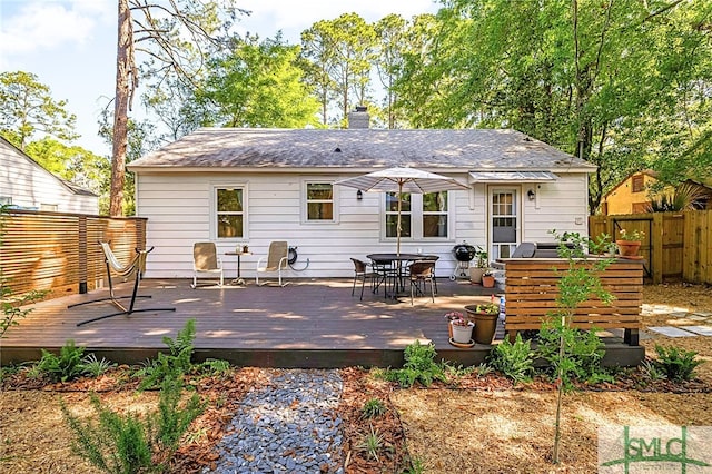 back of property featuring outdoor dining area, a chimney, fence, and a deck