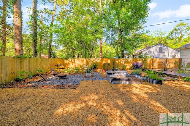 view of yard featuring a fenced backyard, a wooden deck, an outdoor fire pit, and a vegetable garden