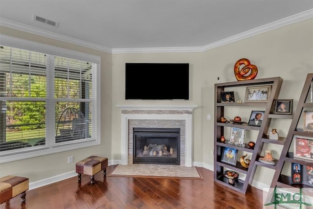 living area featuring a fireplace with flush hearth, baseboards, visible vents, wood finished floors, and ornamental molding