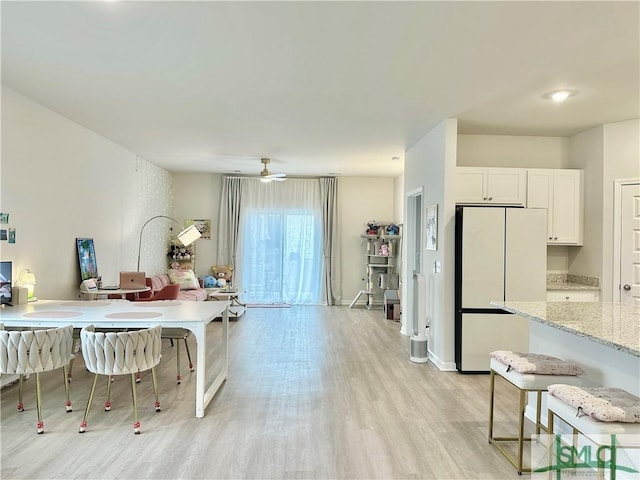 kitchen with a ceiling fan, light wood-type flooring, light stone counters, white cabinets, and freestanding refrigerator