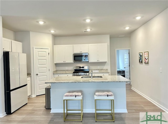 kitchen with a sink, light wood finished floors, appliances with stainless steel finishes, and white cabinets