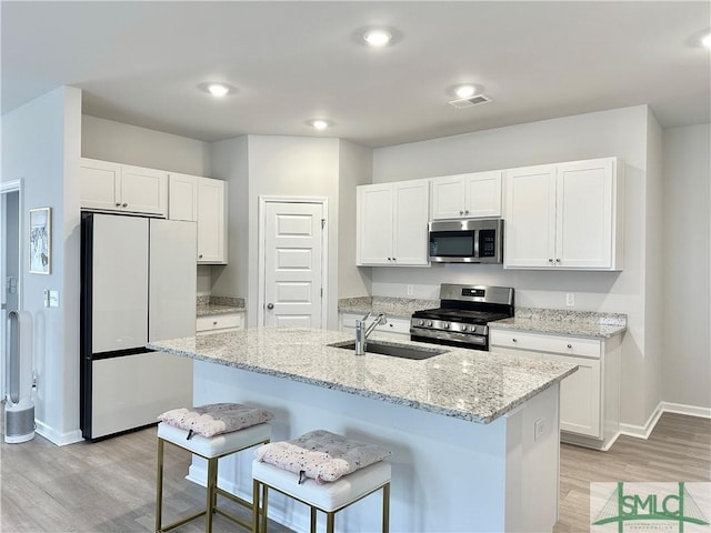 kitchen with baseboards, light wood-type flooring, white cabinetry, a sink, and stainless steel appliances