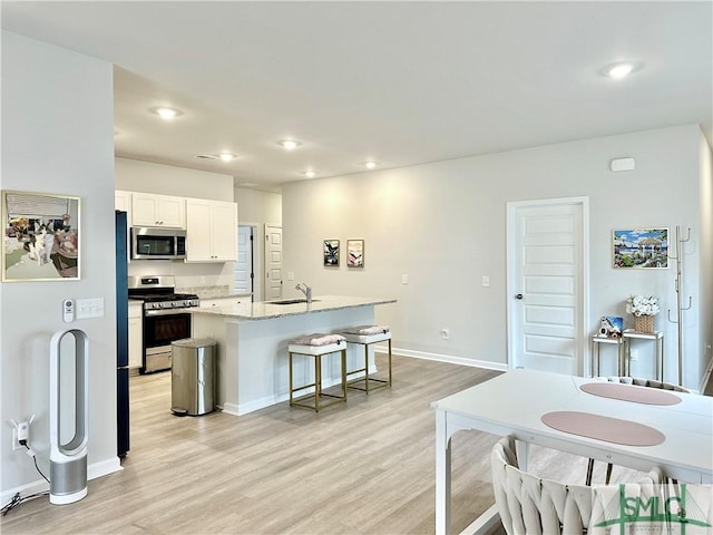 kitchen with light wood-type flooring, a sink, appliances with stainless steel finishes, and a center island with sink