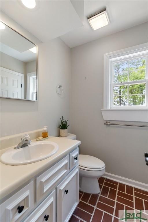 bathroom featuring brick floor, baseboards, vanity, and toilet