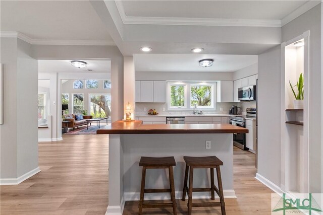kitchen featuring white cabinets, light wood finished floors, a sink, a kitchen bar, and appliances with stainless steel finishes