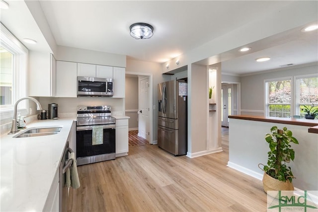 kitchen with white cabinetry, a sink, light wood-style floors, and appliances with stainless steel finishes