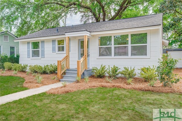 ranch-style home featuring a shingled roof and a front lawn