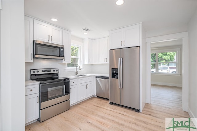 kitchen with a sink, decorative backsplash, stainless steel appliances, white cabinets, and visible vents